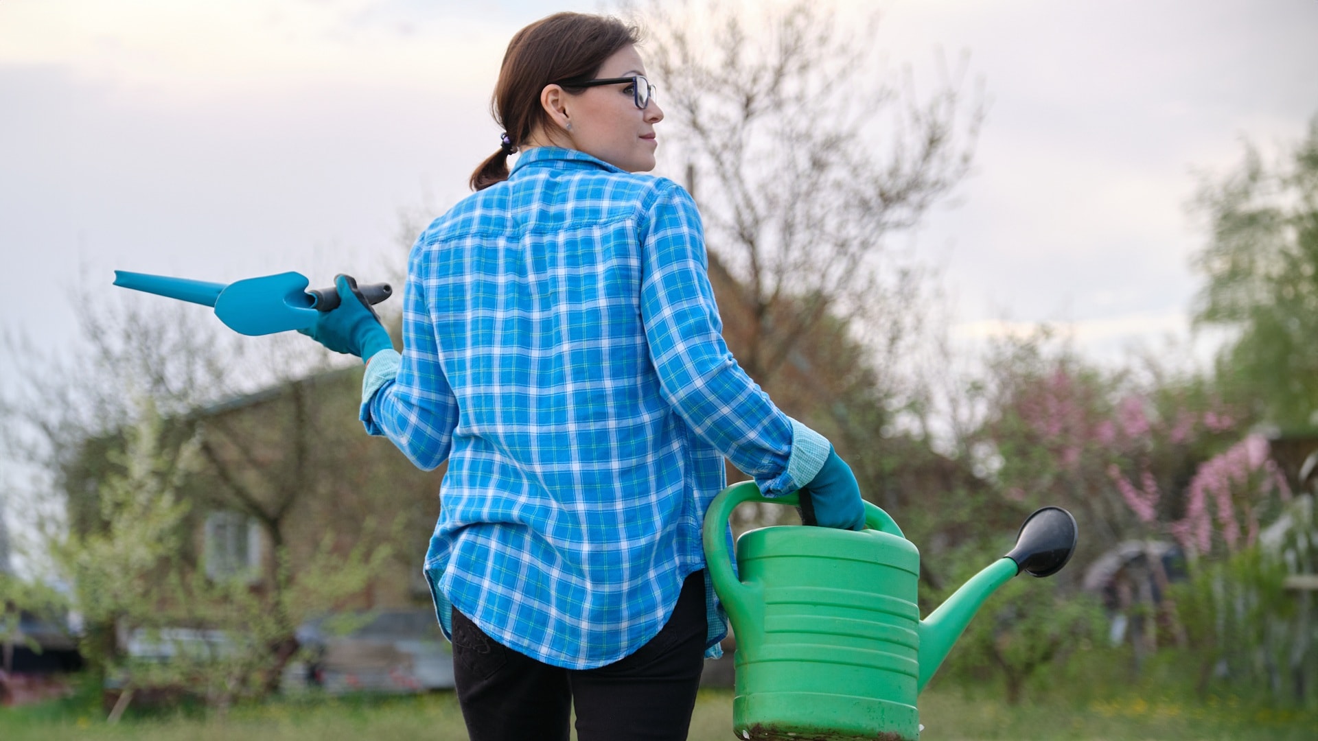 nainen puutarhassa työkalujen ja kastelukannun kera